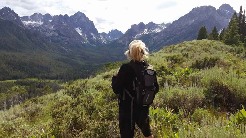 Workamper Lisa Kasefang standing on a mountain top in Idaho looking out with mountains in the distance.