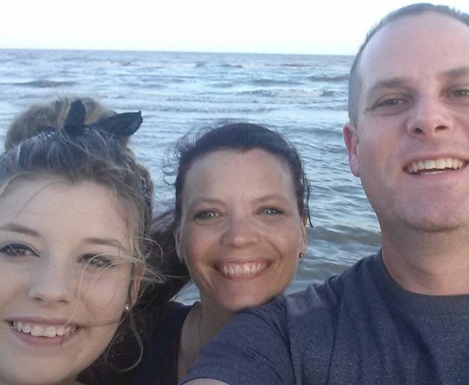 Workampers Chris & Kimberly Travaglino along with their daughter, smiling selfie with water in the background.