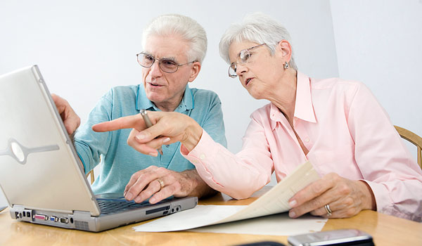 Couple sitting at table working and pointing at laptop.
