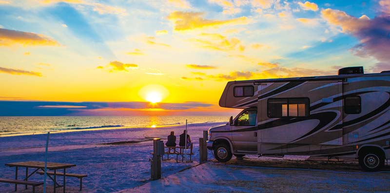 Motorhome on the beach at sunset at Camp Gulf Campground, with a Workamper couple relaxing at a picnic table.