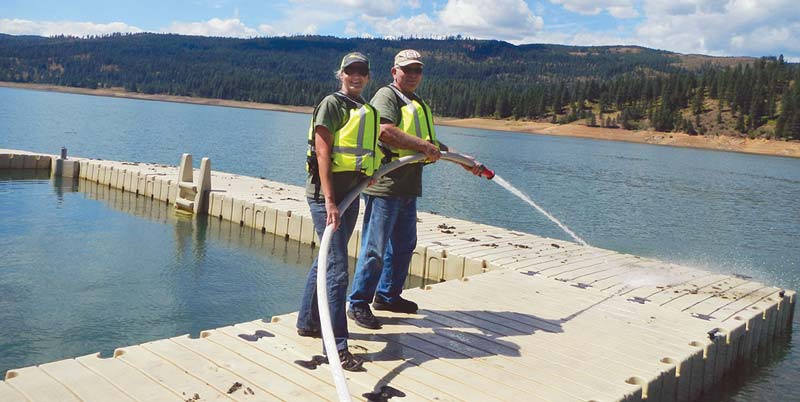 Workampers Lea and Larry Crestman cleaning leaf debris off docks with a fire hose.