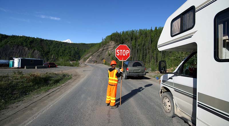 RV stopped at worker holding stop sign, road work.