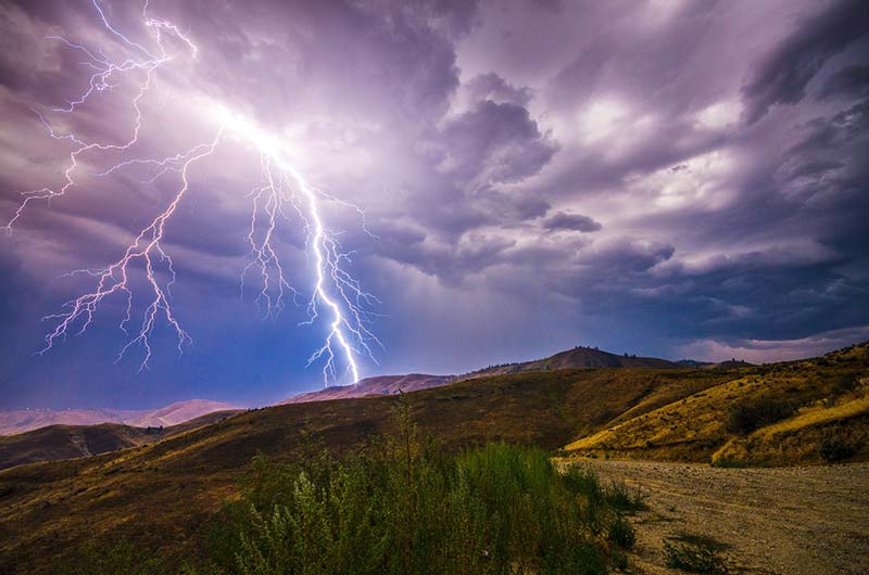 Lighting striking over hills near mountain top.