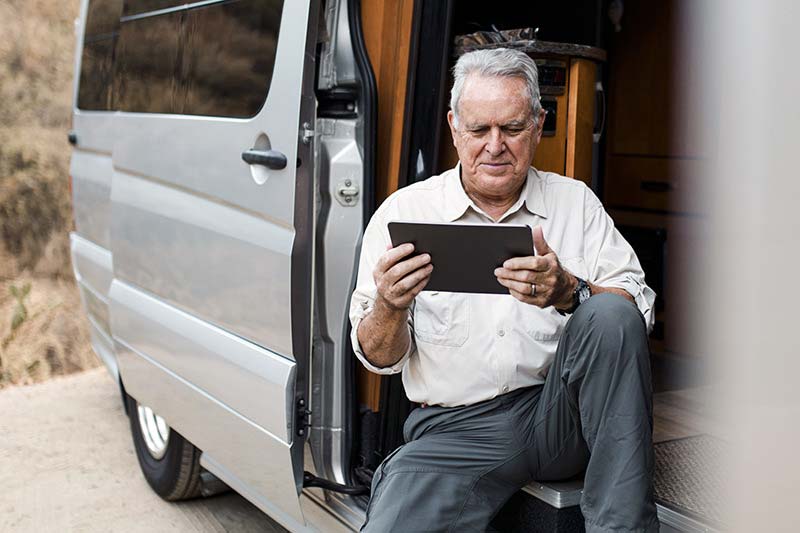 Workamper reviewing a tablet in his van while preparing for a job, illustrating pre-acceptance checklist planning.