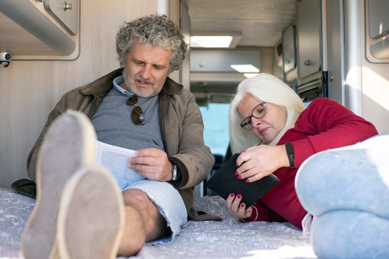 Couple lying on an RV bed reviewing travel plans and working on their budget together.