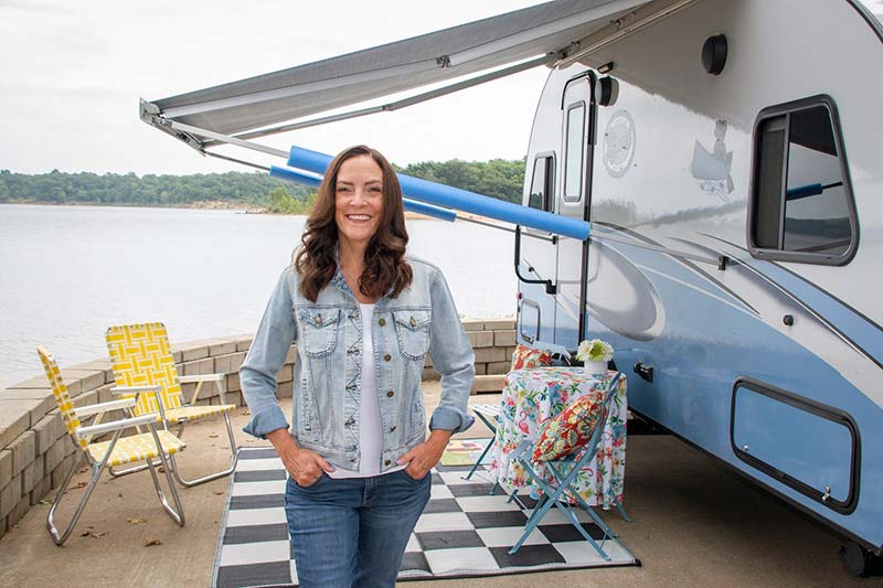Workamper Brenda Pucket outside her RV at a lakeside location, illustrating her journey of turning her RV hobby into a career that empowers others.