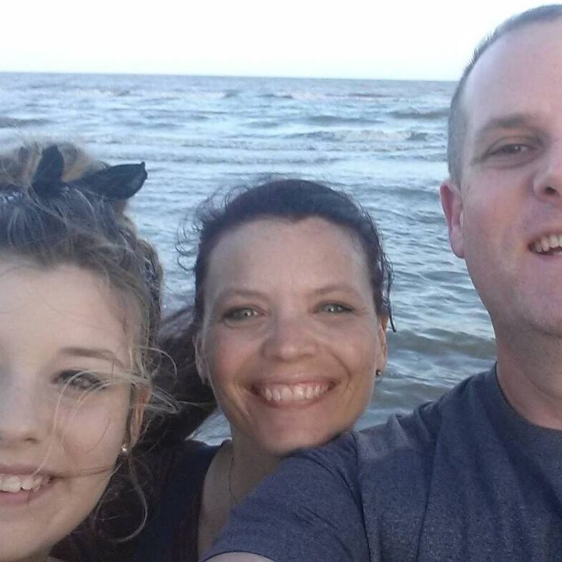 Workampers Chris & Kimberly Travaglino along with their daughter, smiling selfie with water in the background.