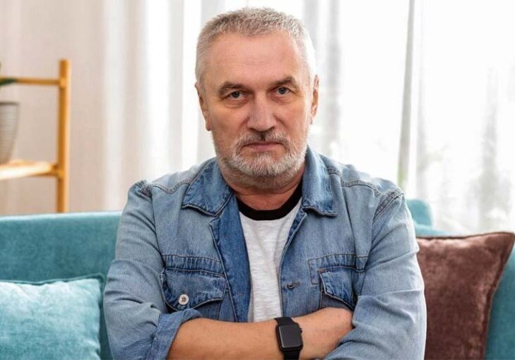 Frustrated man sitting on a couch, arms crossed, appearing upset or contemplative.