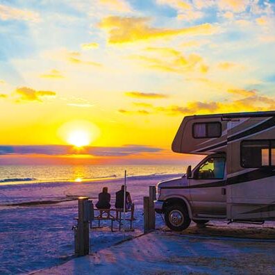 Motorhome on the beach at sunset at Camp Gulf Campground, with a Workamper couple relaxing at a picnic table.