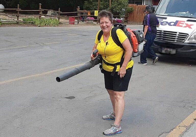 Workamper using leaf blower to clear away leaves from the road in a campground.