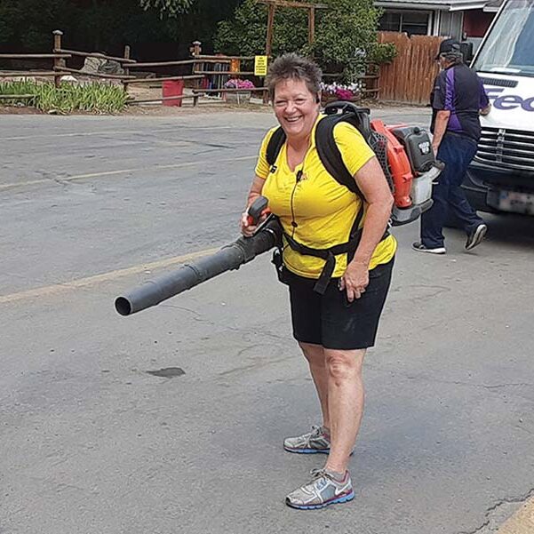 Workamper using leaf blower to clear away leaves from the road in a campground.