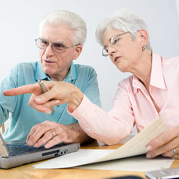 Couple sitting at table working and pointing at laptop.