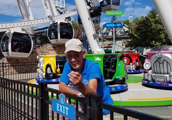 Workamper smiling for a photo at an amusement park with a ferris wheel and colorful rides behind them