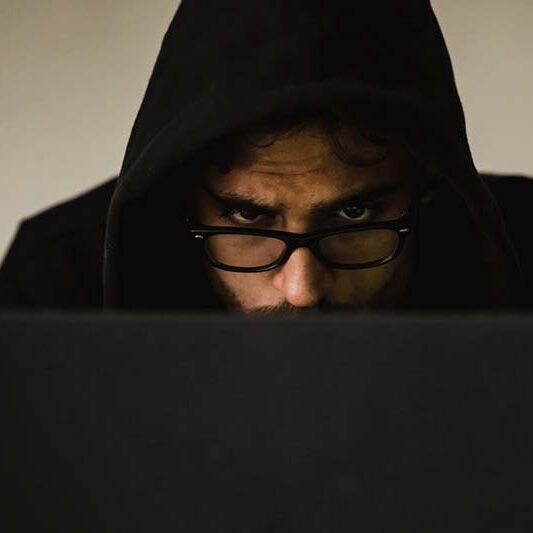 Man in a hoodie concentrating at a computer, representing researching or spotting Workamper scams.