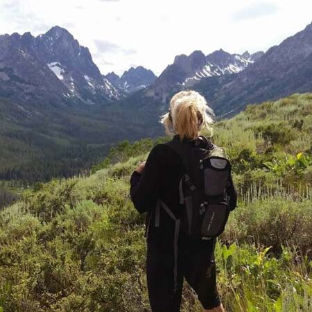 Workamper Lisa Kasefang standing on a mountain top in Idaho looking out with mountains in the distance.