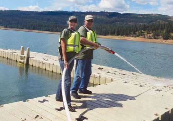Workampers Lea and Larry Crestman cleaning leaf debris off docks with a fire hose.