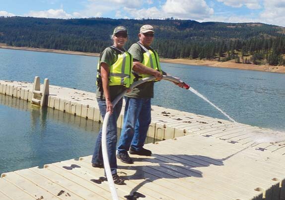 Workampers Lea and Larry Crestman cleaning leaf debris off docks with a fire hose.
