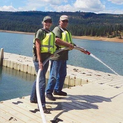 Workampers Lea and Larry Crestman cleaning leaf debris off docks with a fire hose.