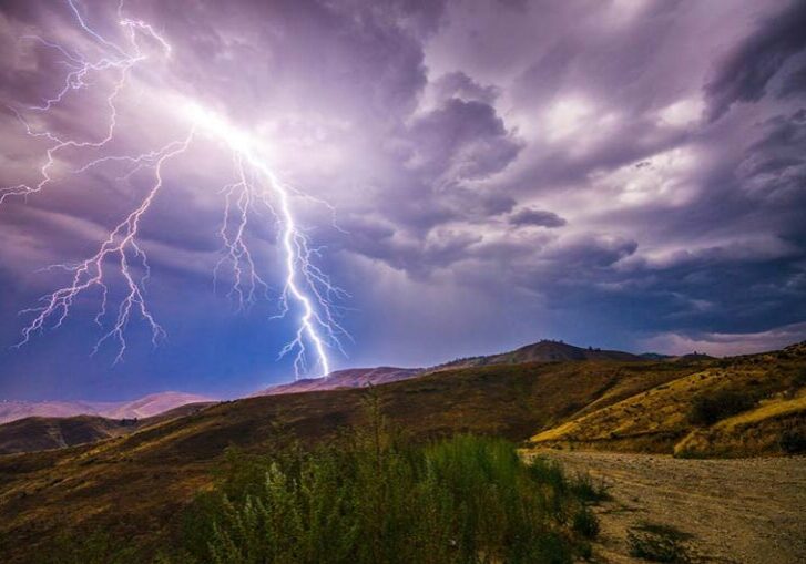 Lighting striking over hills near mountain top.