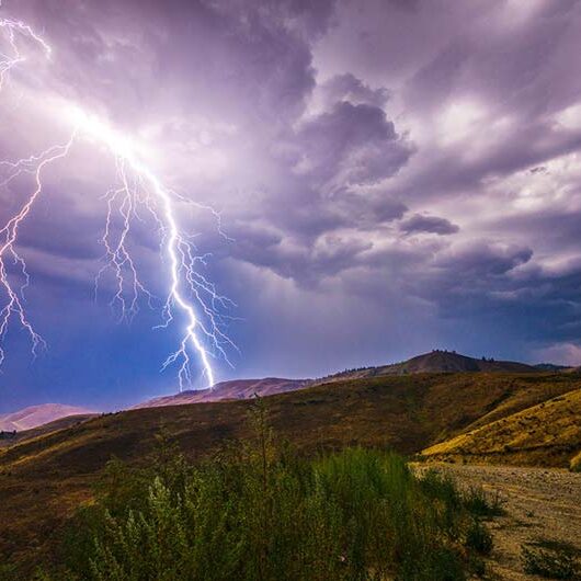 Lighting striking over hills near mountain top.