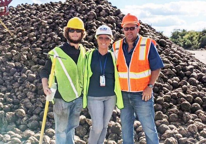 Workampers with Express Employment posing in front of a mountain of sugar beets at the Michigan Beet Harvest, representing seasonal agricultural jobs for RVers.