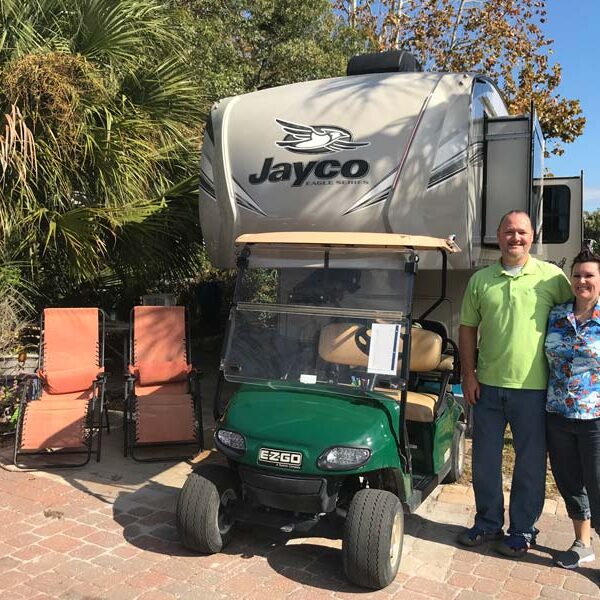 Workampers posing in front of Jayco 5th wheel at Camp Gulf RV site with golf cart to the side.
