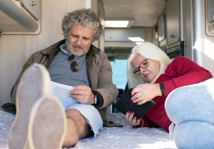 Couple lying on an RV bed reviewing travel plans and working on their budget together.