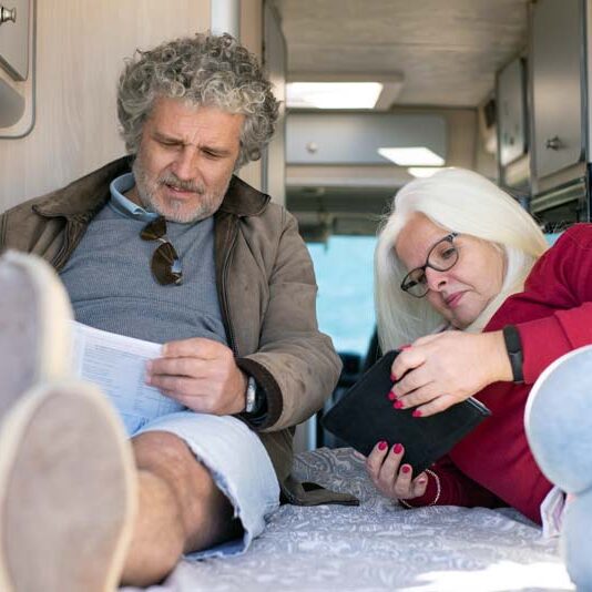Couple lying on an RV bed reviewing travel plans and working on their budget together.