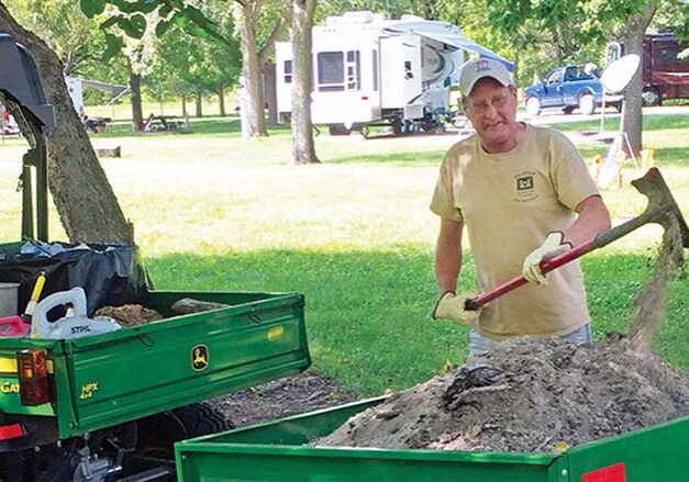 Workamper Terry Curry tossing dirt onto a dirt pile in a trailer attached to a UTV.