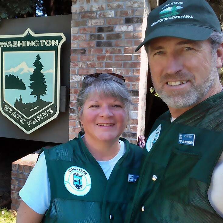 Washington State Park Volunteers, Workampers Jon & Sherry Hockersmith smiling in front of Washington State Parks sign.