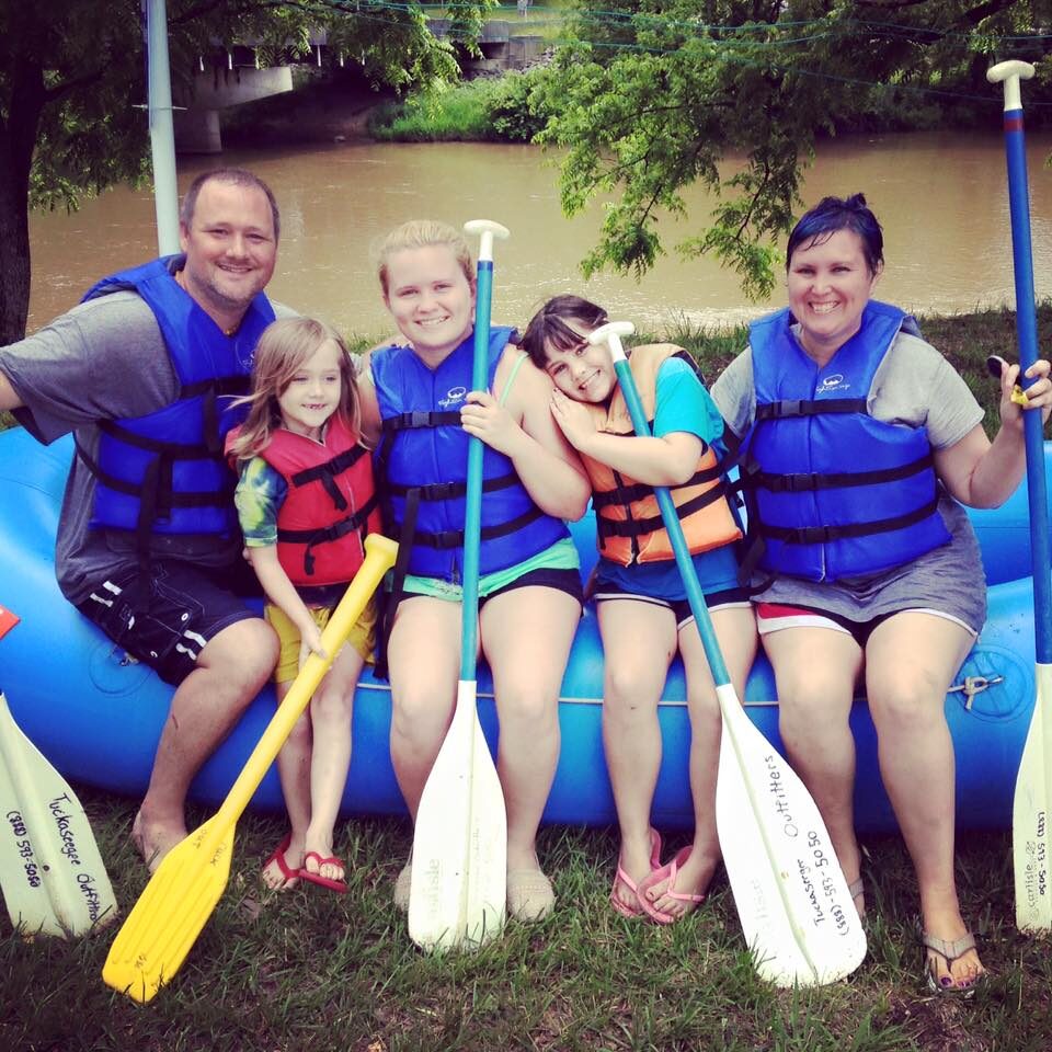 Full-time RVing Mooney family, posing on blue raft with river in the background.