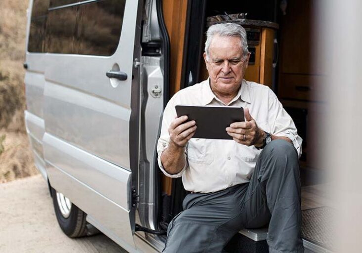 Workamper reviewing a tablet in his van while preparing for a job, illustrating pre-acceptance checklist planning.