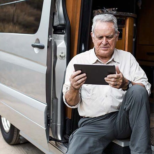 Workamper reviewing a tablet in his van while preparing for a job, illustrating pre-acceptance checklist planning.
