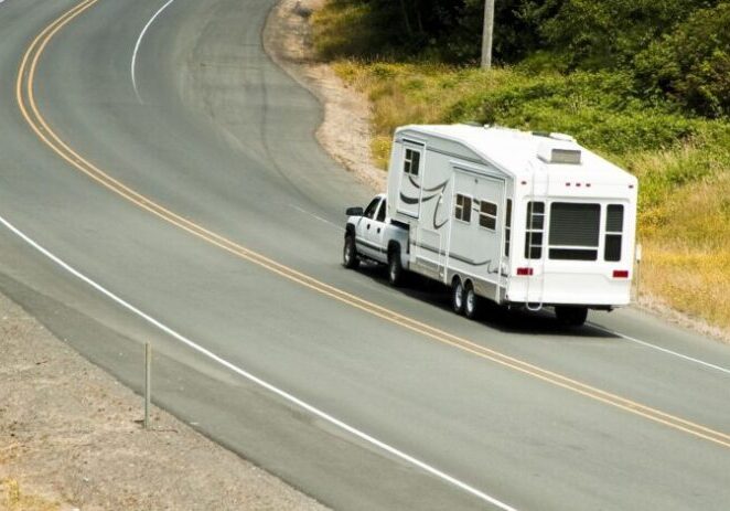 Pickup truck towing a 5th wheel trailer on the highway.