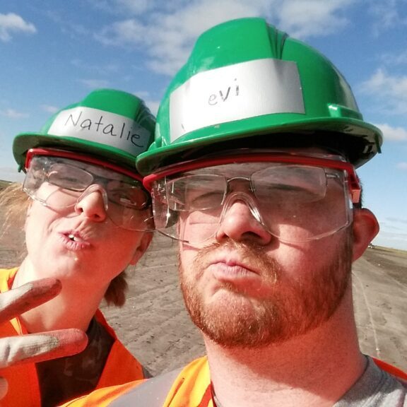 Workampers Levi and Natalie Henley taking a selfie wearing hard hats and safety vests at sugar beet harvest.